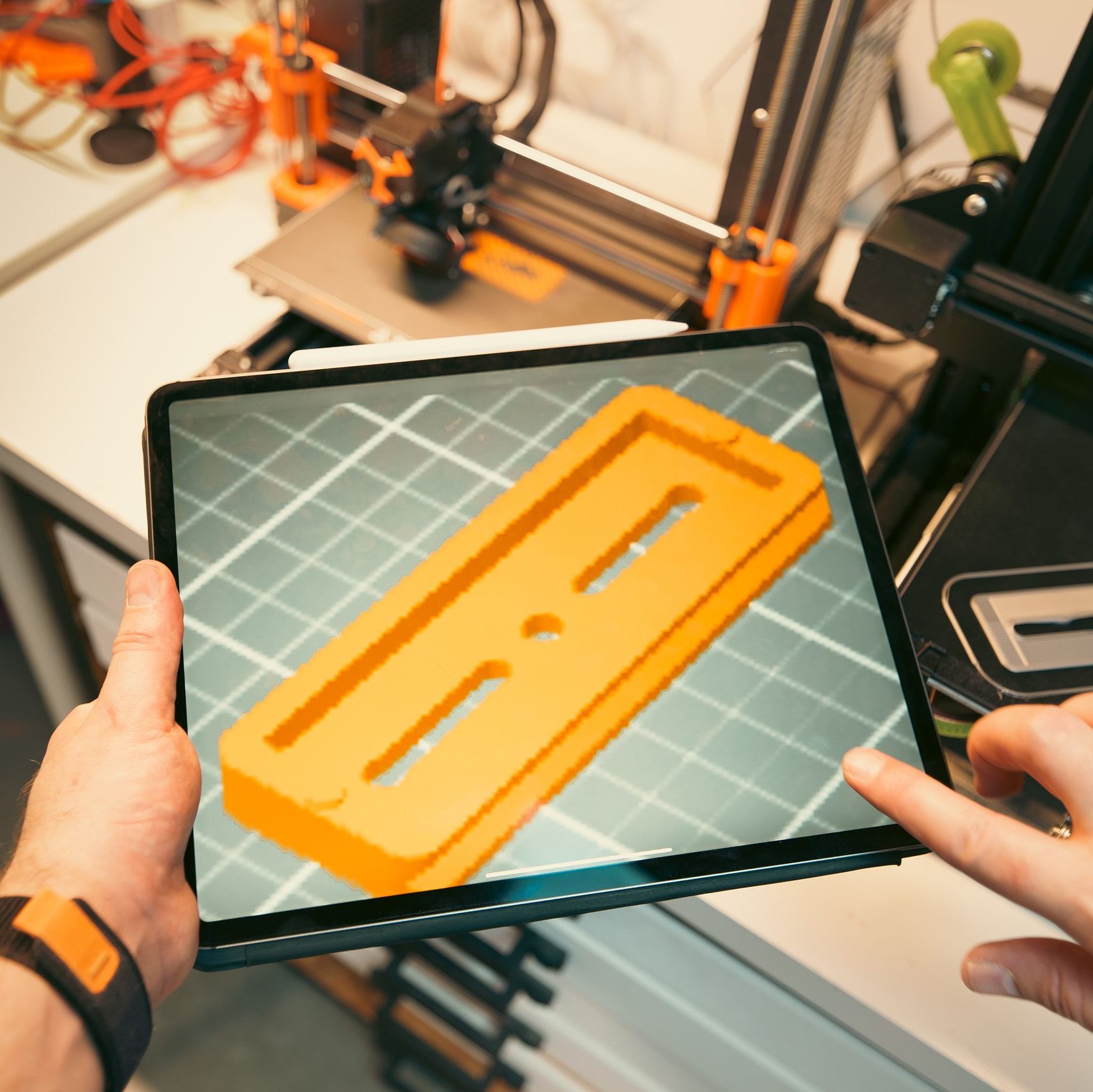 A person uses a tablet to view a 3D model prototype in a workshop equipped with 3D printers.