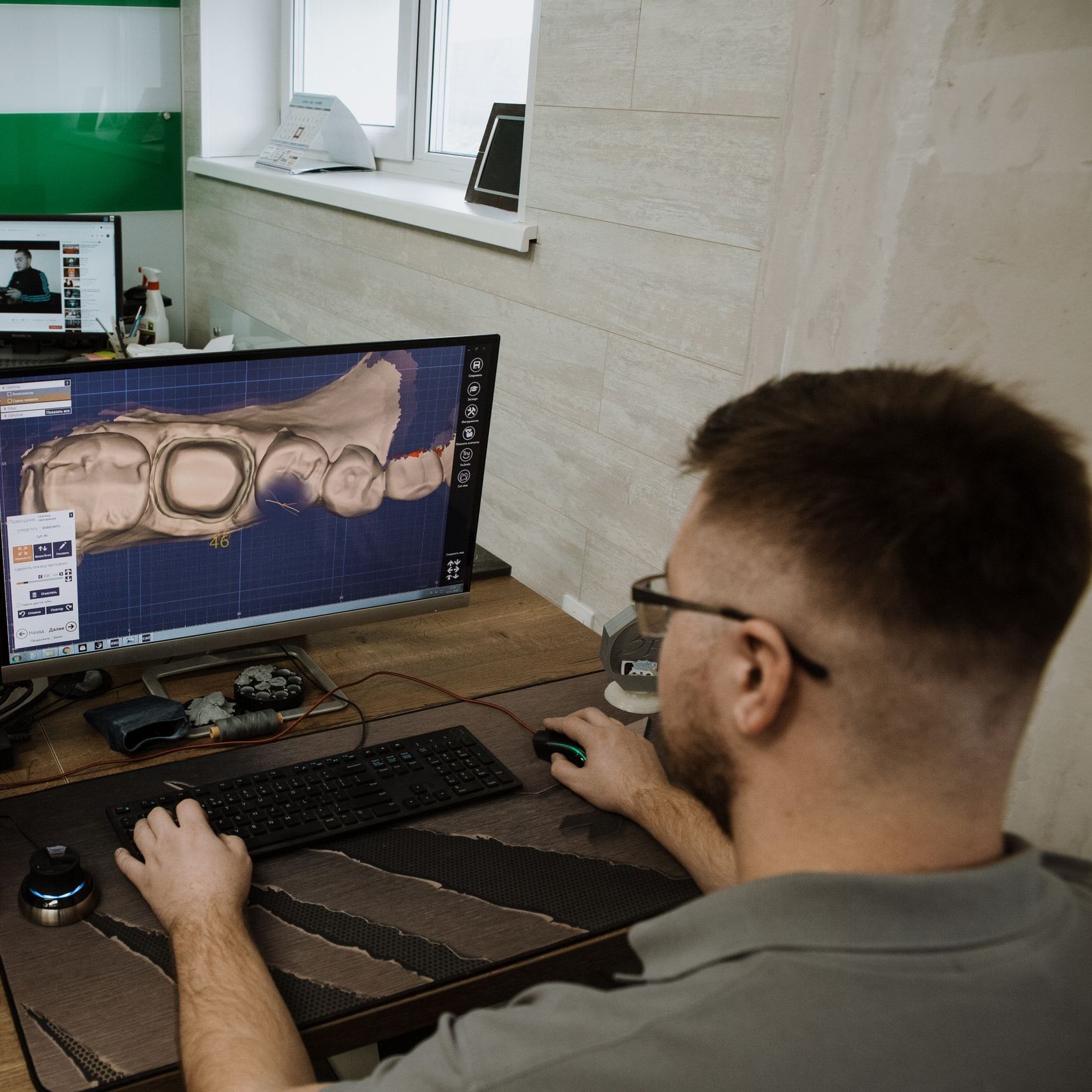 Back view of anonymous male programmer sitting at table and creating 3d model of teeth while working in modern dental laboratory